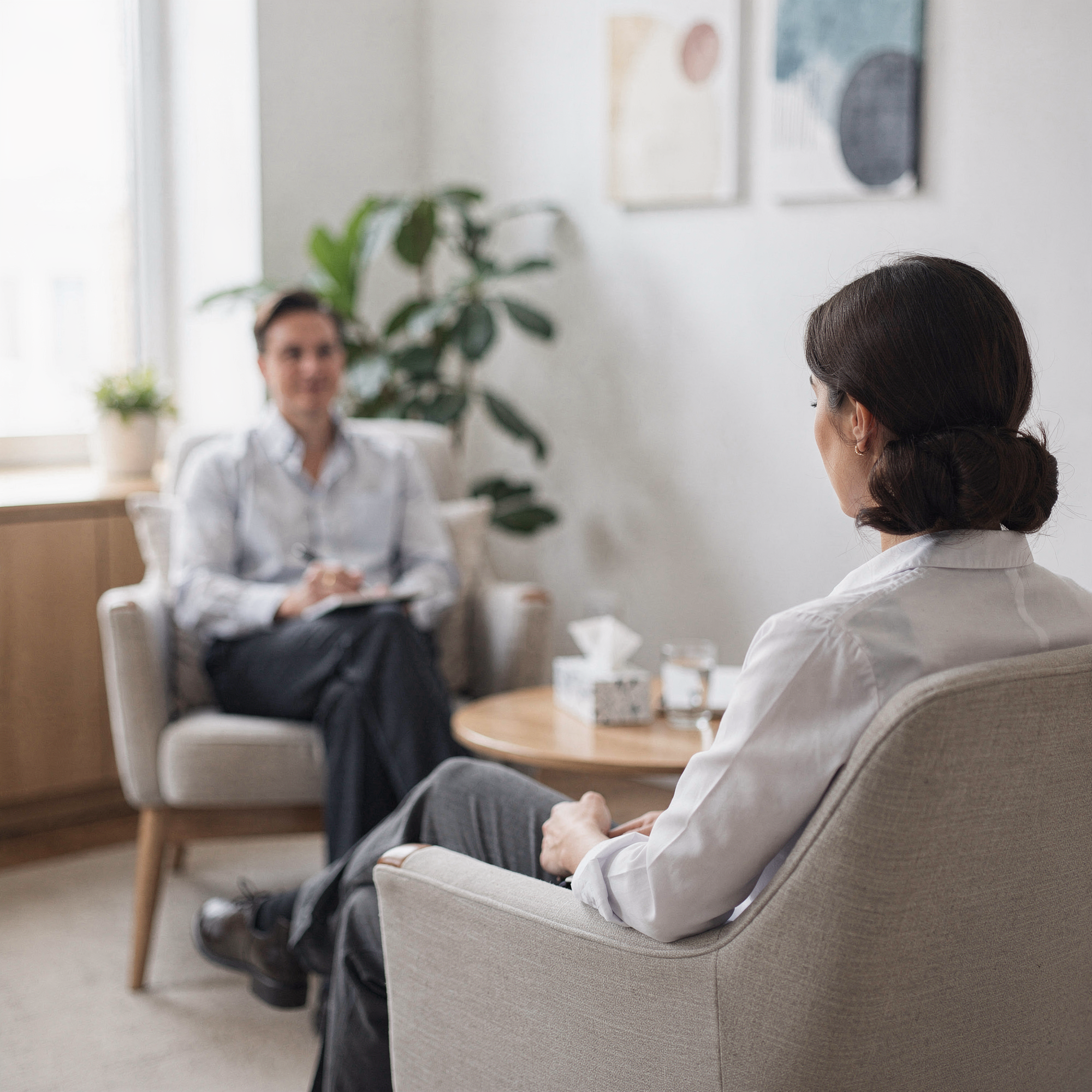 Mental health provider taking notes during a therapy session with a patient in a bright, plant-filled office